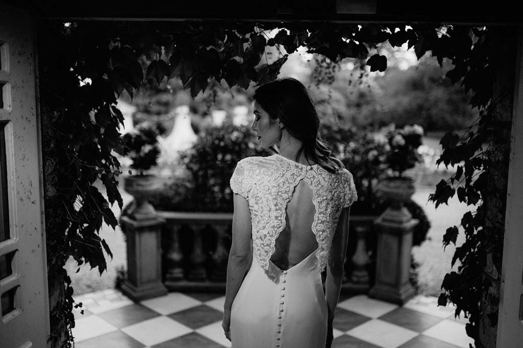 The back of the bride’s lace gown under the vine-covered walkway